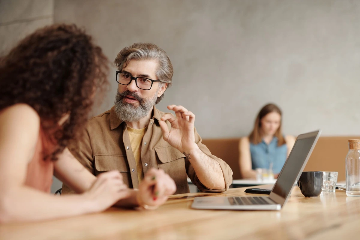 Dos profesionales conversando en una mesa de trabajo con un portátil