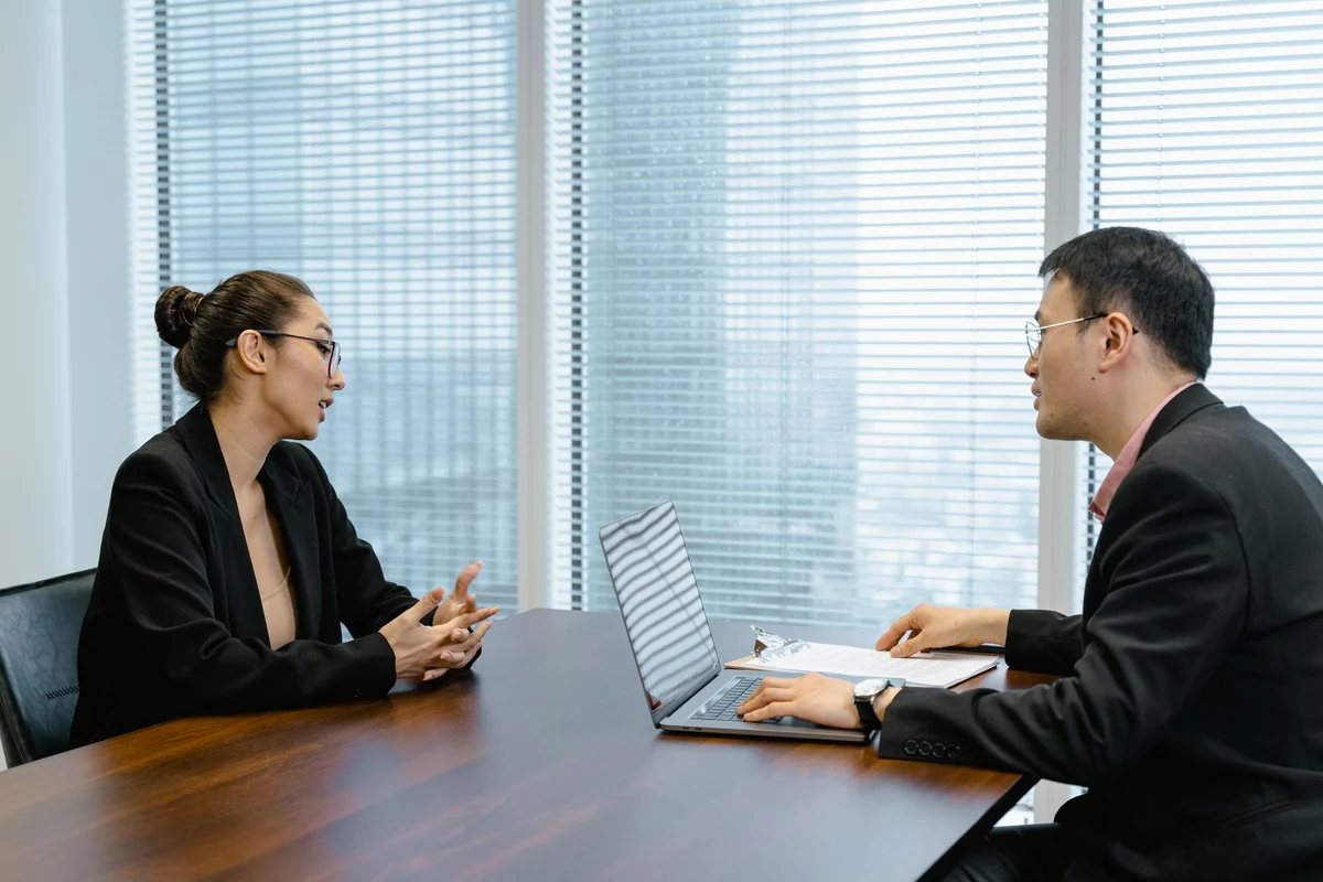 Dos profesionales conversan frente a frente en una mesa de reuniones de oficina
