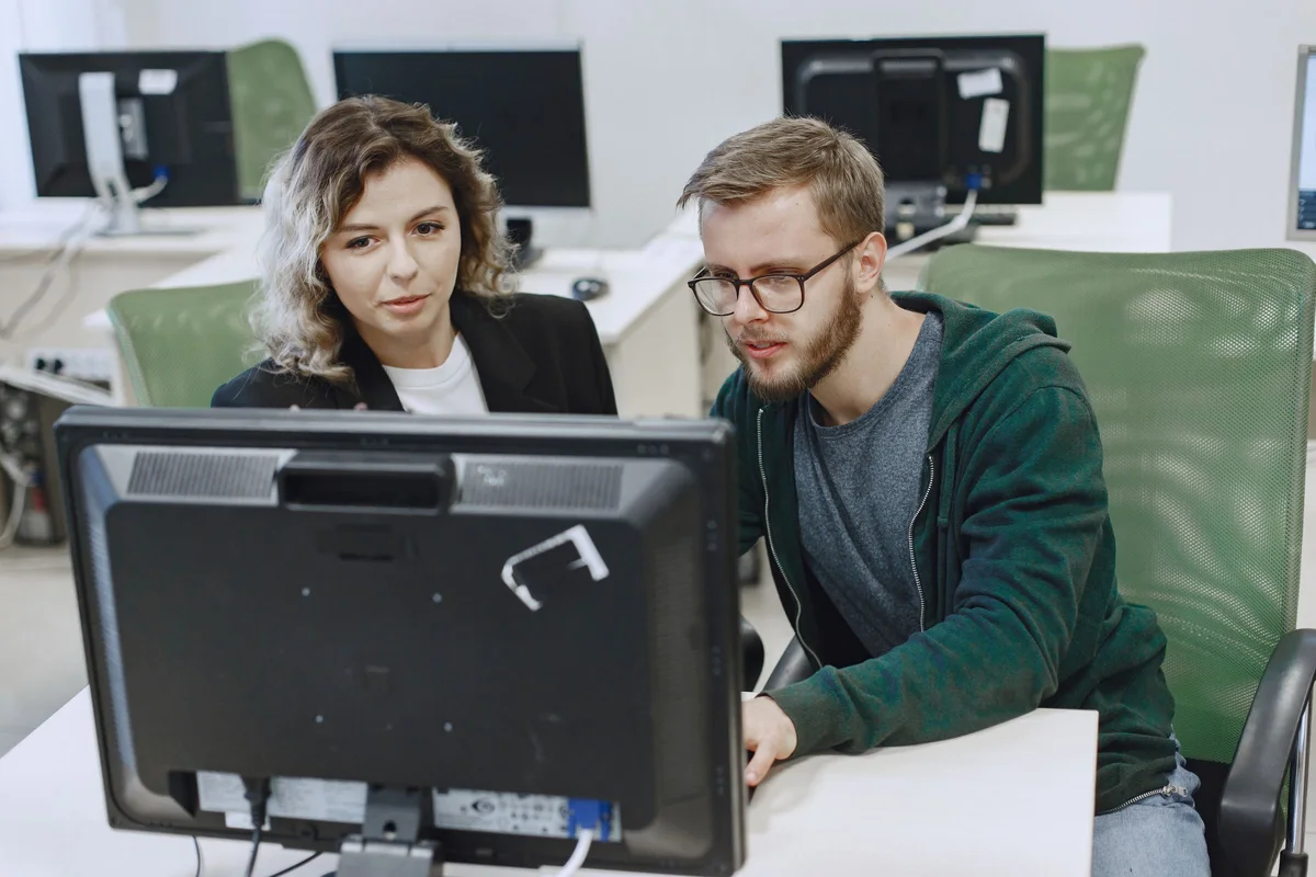 Dos companeros de un equipo comercial B2B revisando juntos el estado de sus leads frente a la pantalla del ordenador