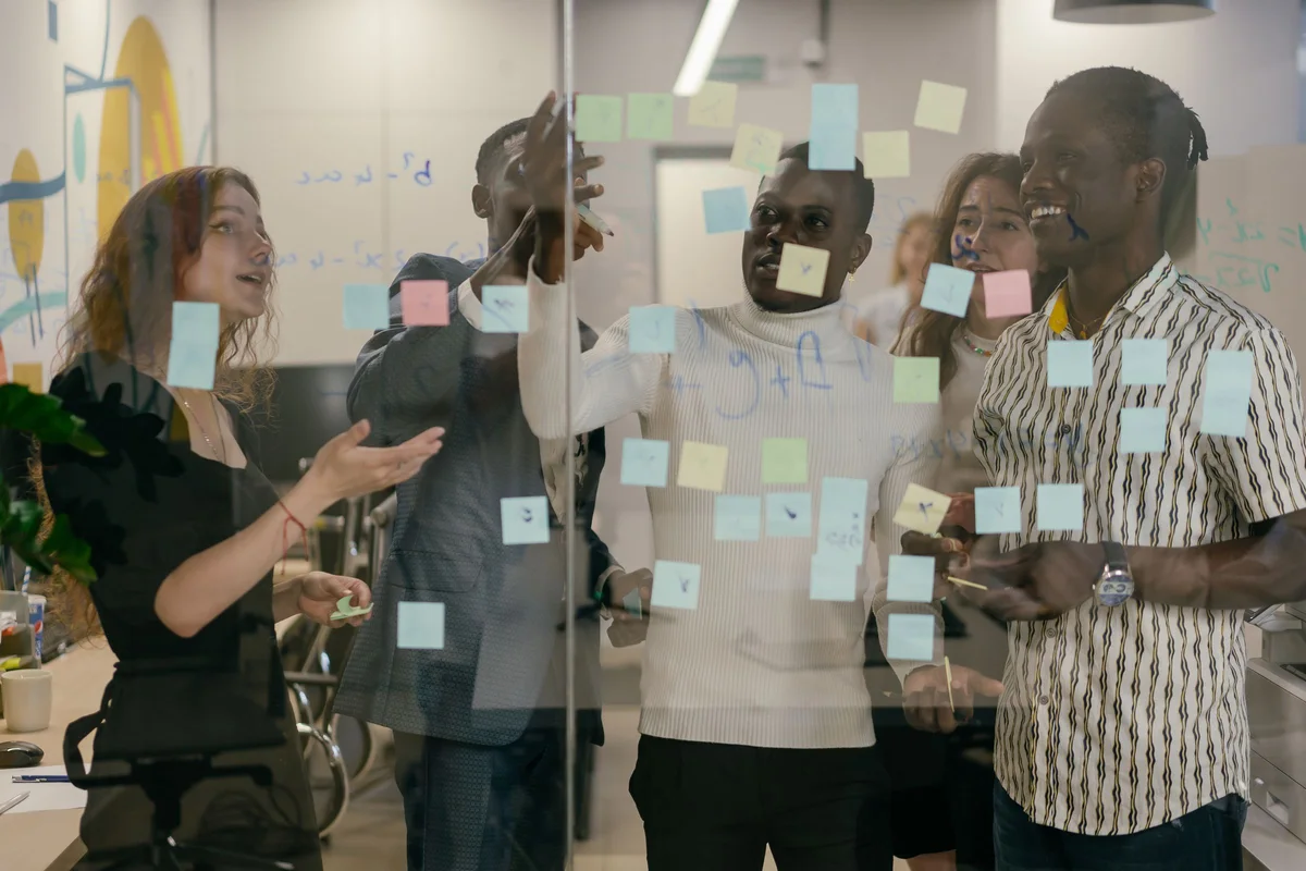 Equipo de ventas planificando su proceso comercial con notas adhesivas en una pared de cristal