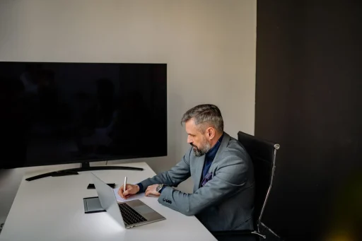 Profesional de ventas B2B tomando notas junto a su portatil en una oficina para hacer seguimiento de sus leads