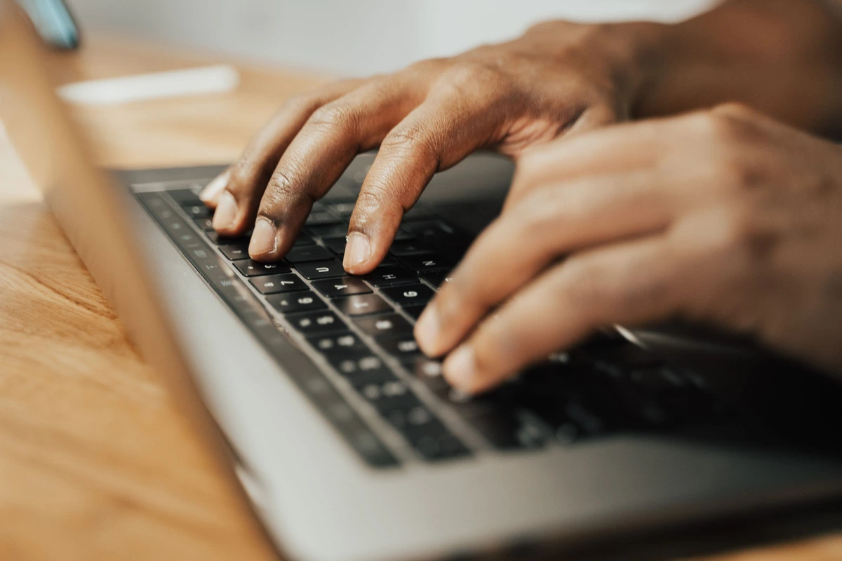 Manos escribiendo en el teclado de un portátil sobre un escritorio de madera clara