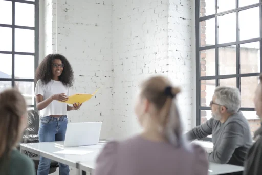 Profesional de pie dirigiendo una reunion con su equipo sentado alrededor de la mesa en una oficina luminosa