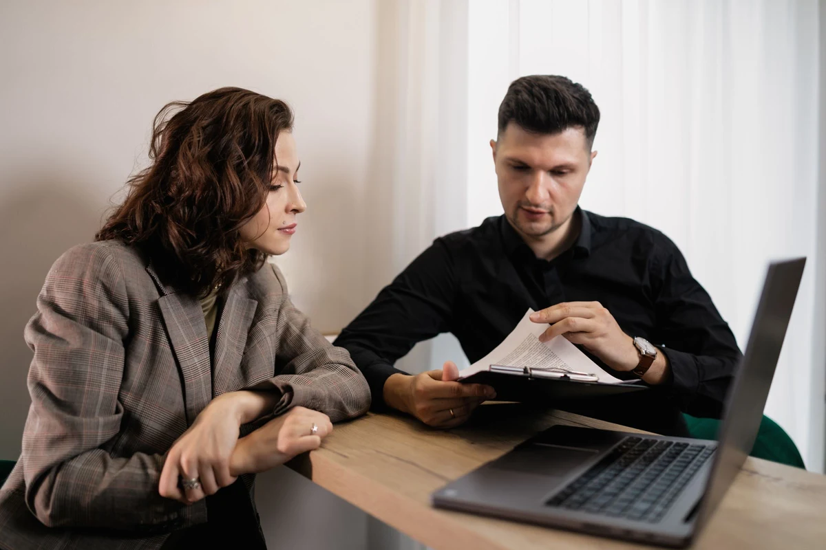 Manager y comercial revisando juntos un informe impreso en una reunion uno a uno, con un portatil abierto al lado